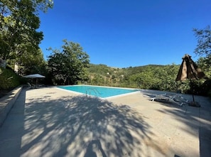 Ein Pool mit Betonumrandung, umgeben von Bäumen und blauem Himmel.