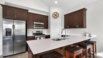 Una cocina moderna con electrodomésticos de acero inoxidable, una isla grande con taburetes de bar y armarios de madera oscura.