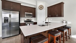 Una cocina moderna con electrodomésticos de acero inoxidable, armarios de madera oscura, una isla grande con taburetes y un elemento decorativo en la pared.