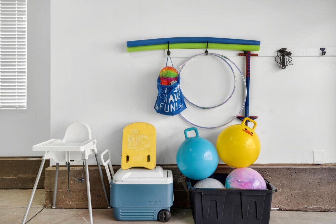 Una habitación con una pared blanca, una silla blanca, un enfriador azul, un enfriador amarillo, un bote de basura negro y una tabla de surf.