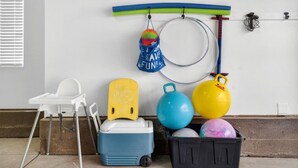 Una habitación con una pared blanca, una silla blanca, un enfriador azul, un enfriador amarillo, un bote de basura negro y una tabla de surf.