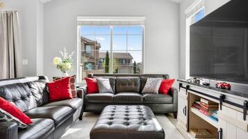 A living room with a large window, a leather sofa set, a television, and a bookshelf.