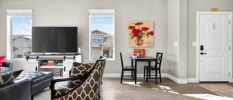 A living room with a sofa, a television, a dining table with chairs, and a painting on the wall.