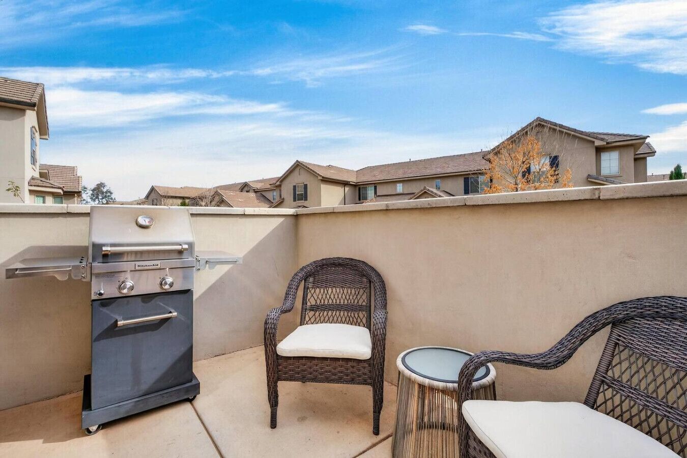 A patio with a grill, wicker chairs, and a small table.