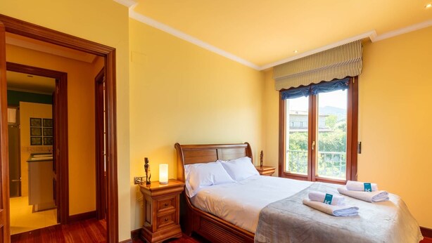 Een hotelkamer met een houten bed, een nachtkastje met een lamp, een raam met uitzicht en een deur naar een badkamer.