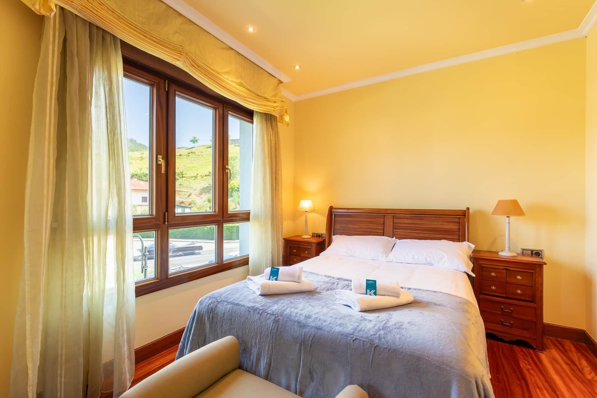 A hotel room with a bed, bedside tables, a chair, a window with curtains, and a view of the outdoors.