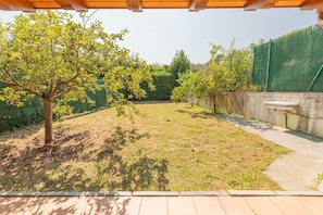 A covered outdoor area with a paved walkway, a tree, and a green fence.