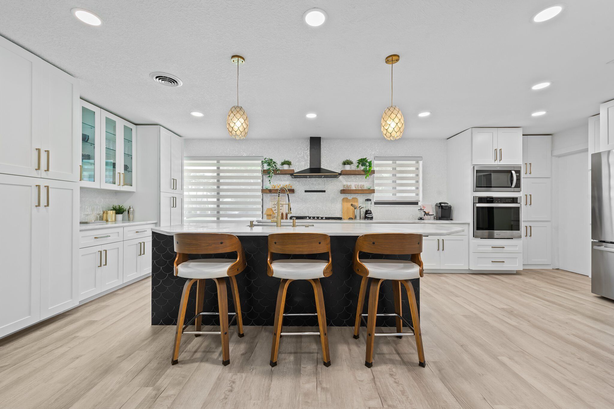 Une cuisine moderne avec des meubles blancs, un îlot central doté de tabourets, des appareils électroménagers intégrés et un éclairage suspendu.