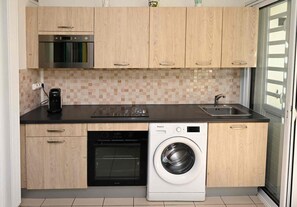 Cocina compacta equipada con microondas, lavavajillas y lavadora, armarios de madera y salpicadero de azulejos.