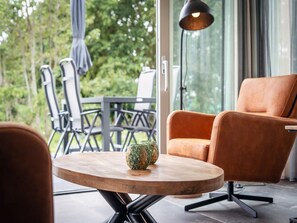 A modern interior with a round wooden table, a single orange chair, and a view of greenery outside. - Pet-free Country House With Sauna (De Koog)