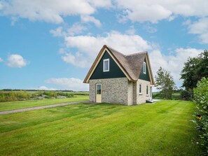A two-story house with a stone facade and a steeply pitched roof, surrounded by a well-maintained lawn and trees. - Pet-free Country House With Sauna (De Koog)