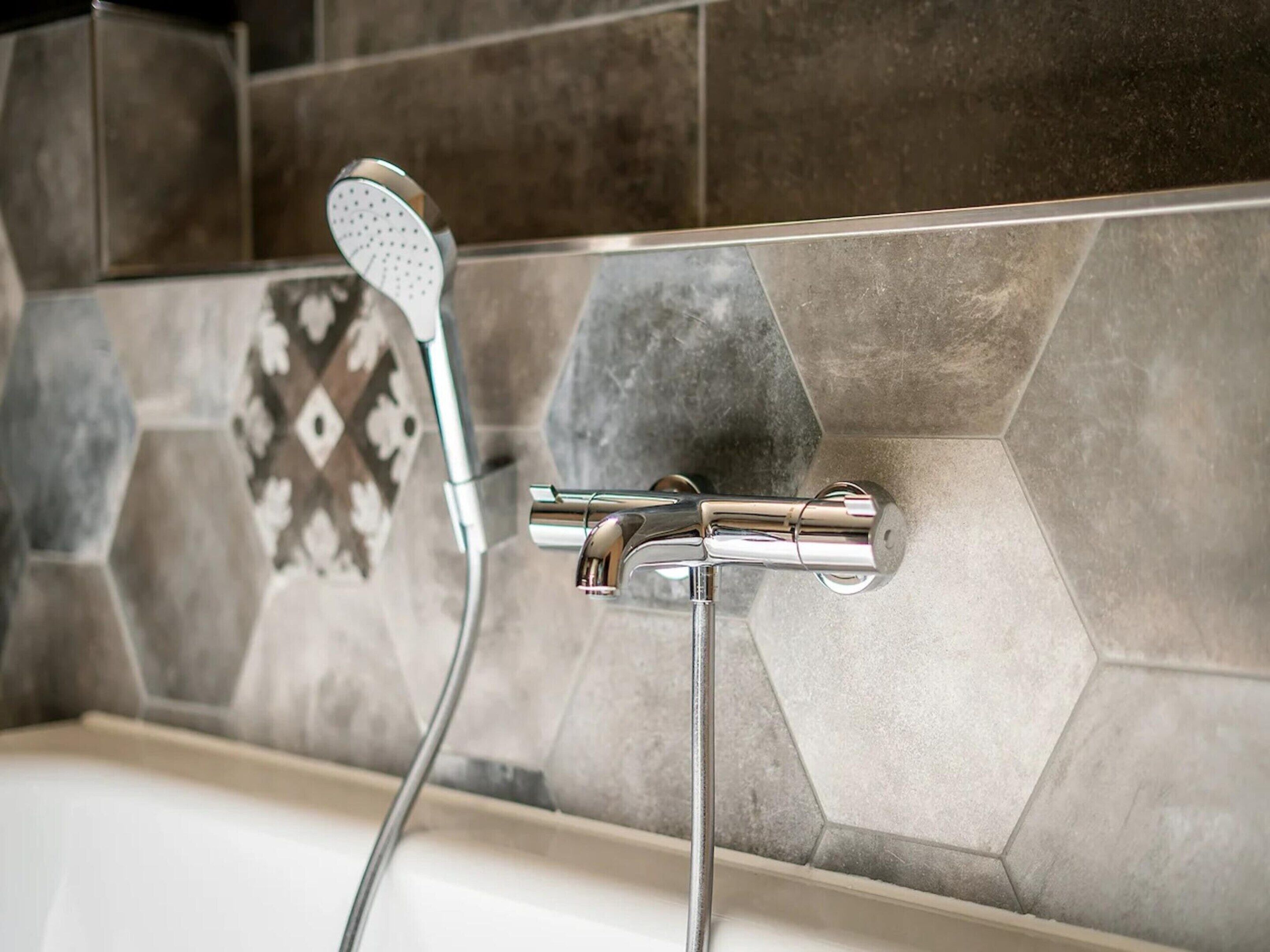 A bathroom with a shower head and faucet mounted on a tiled wall.