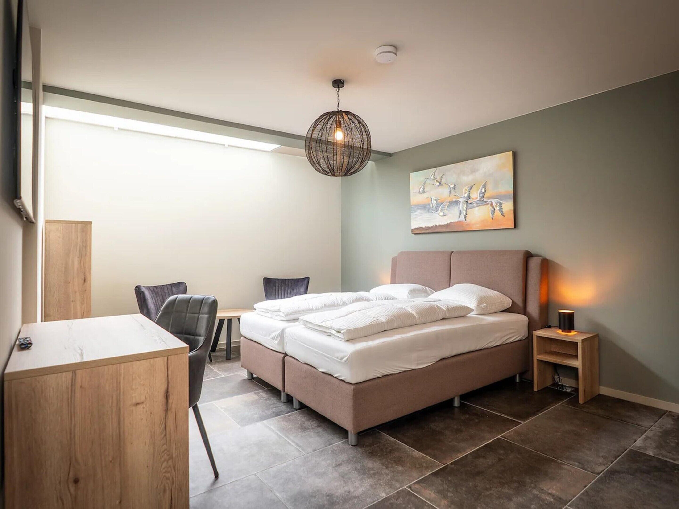 Une chambre à coucher avec un lit, un bureau, une chaise, une table de chevet et un tableau au mur.