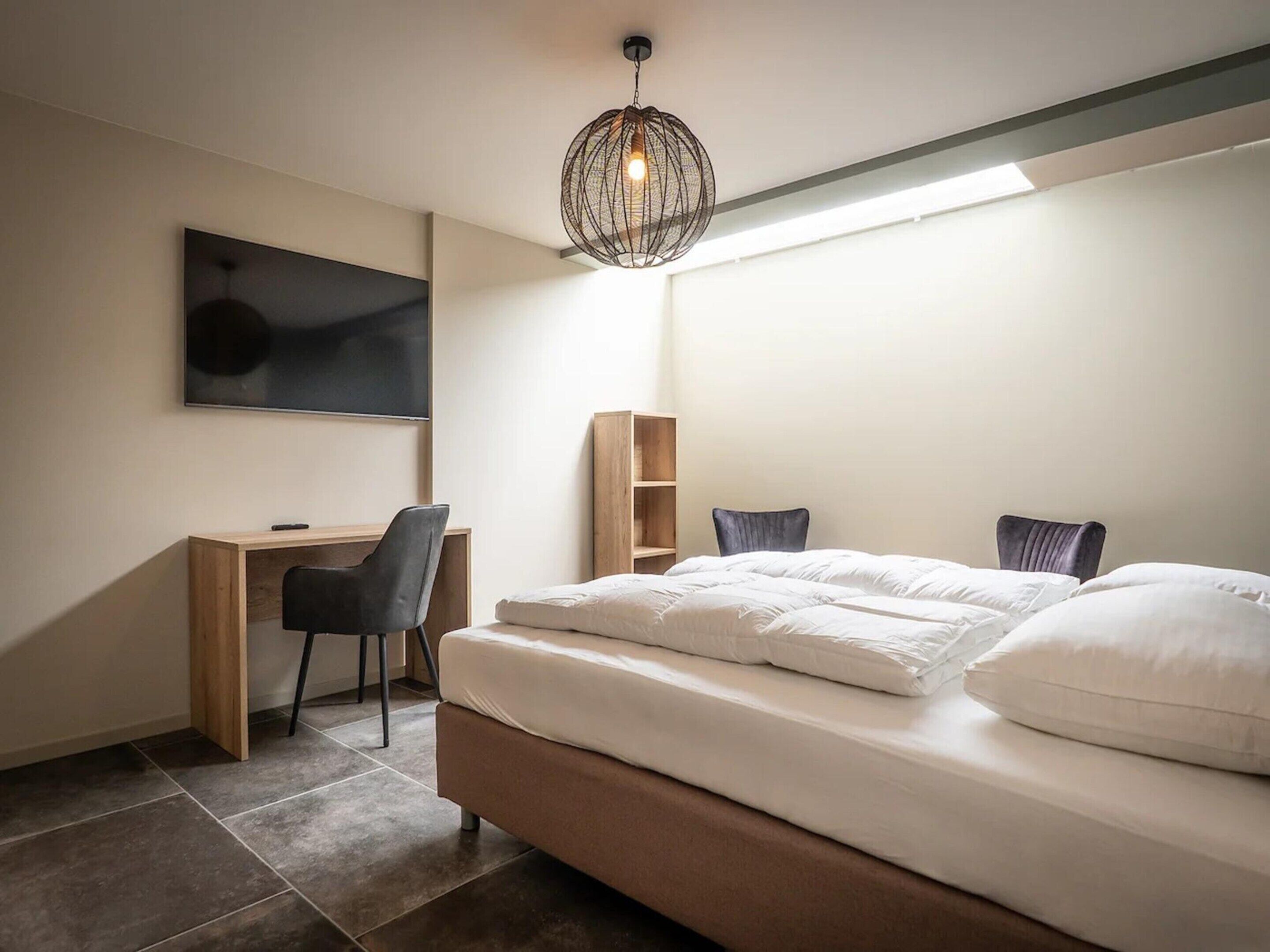 Una camera da letto con un letto, una scrivania, una sedia, una televisione e una lampada a sospensione.