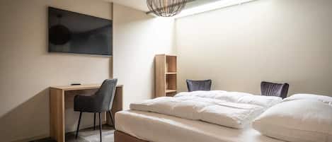 A bedroom with a bed, a desk, a chair, a television, and a hanging light fixture.
