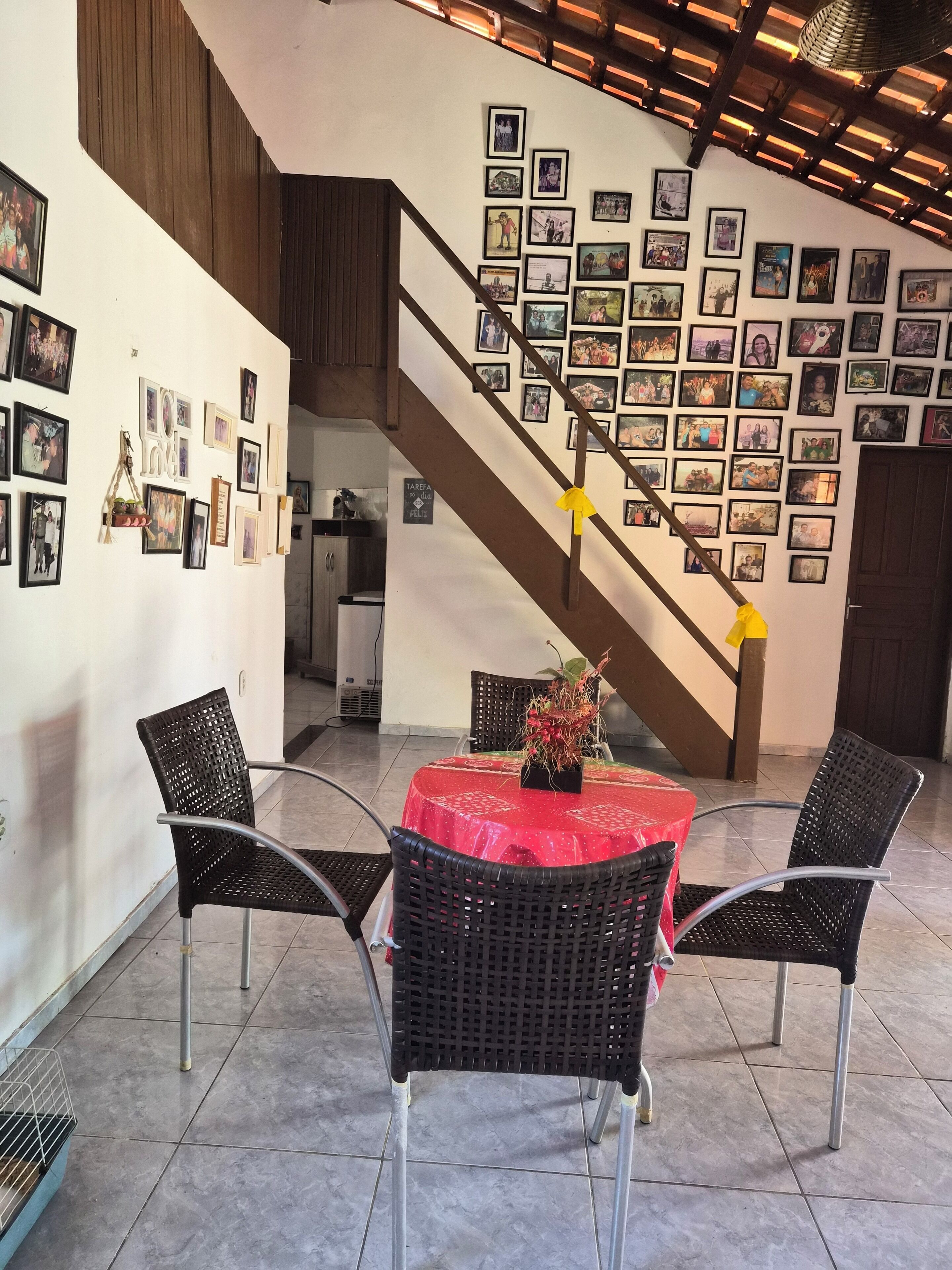 A dining area with a red tablecloth, black wicker chairs, and a staircase with photos on the wall.