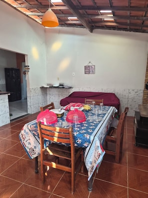 A dining area with a table set for four, covered with a floral tablecloth, surrounded by wooden chairs. - 2-bedroom and 4-suits house in beautiful Luís Correia with cool ocean breeze (Luís Correia)