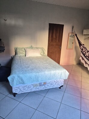 Ein Bett mit gesteppter Matratze, eine Holztür und eine Hängematte.