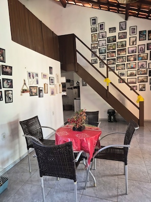 A dining area with a table covered in a red tablecloth, surrounded by black wicker chairs. A staircase with yellow handrails leads to a wall adorned with numerous framed photographs. - 2-bedroom and 4-suits house in beautiful Luís Correia with cool ocean breeze (Luís Correia)