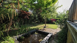 Um jardim com lago, cerca de madeira e diversas plantas.