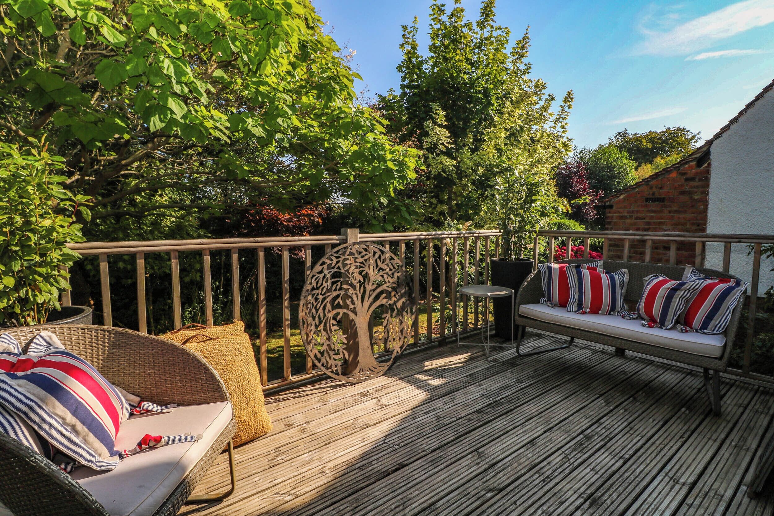 A wooden deck with outdoor furniture, including a wicker chair and a sofa with striped cushions.