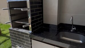 An outdoor kitchen with a built-in grill, a sink, and a tiled backsplash. - House 18 | Private Pool, Gourmet Area and 4 Suites - Near the City Center. (Barreirinhas)