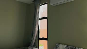 A hotel room with two beds, a window with curtains, an air conditioning unit, and a small table.