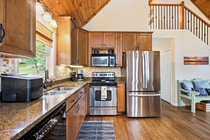 A modern kitchen with wooden cabinets, stainless steel appliances, a granite countertop, and a view of the outdoors. - Welcoming The Sinclair Hideaway (Sparta)