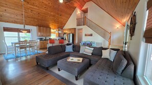 Ein geräumiges Wohnzimmer mit einer großen Eckcouch, einem Essbereich mit Tisch und Stühlen, einer Küche mit Holzausstattung und einer Treppe, die in einen oberen Bereich führt.