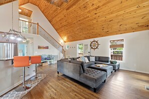Ein geräumiger Wohnbereich mit Holzboden, einer Wendeltreppe, einer modernen Küche und einem großen, grauen Ecksofa.