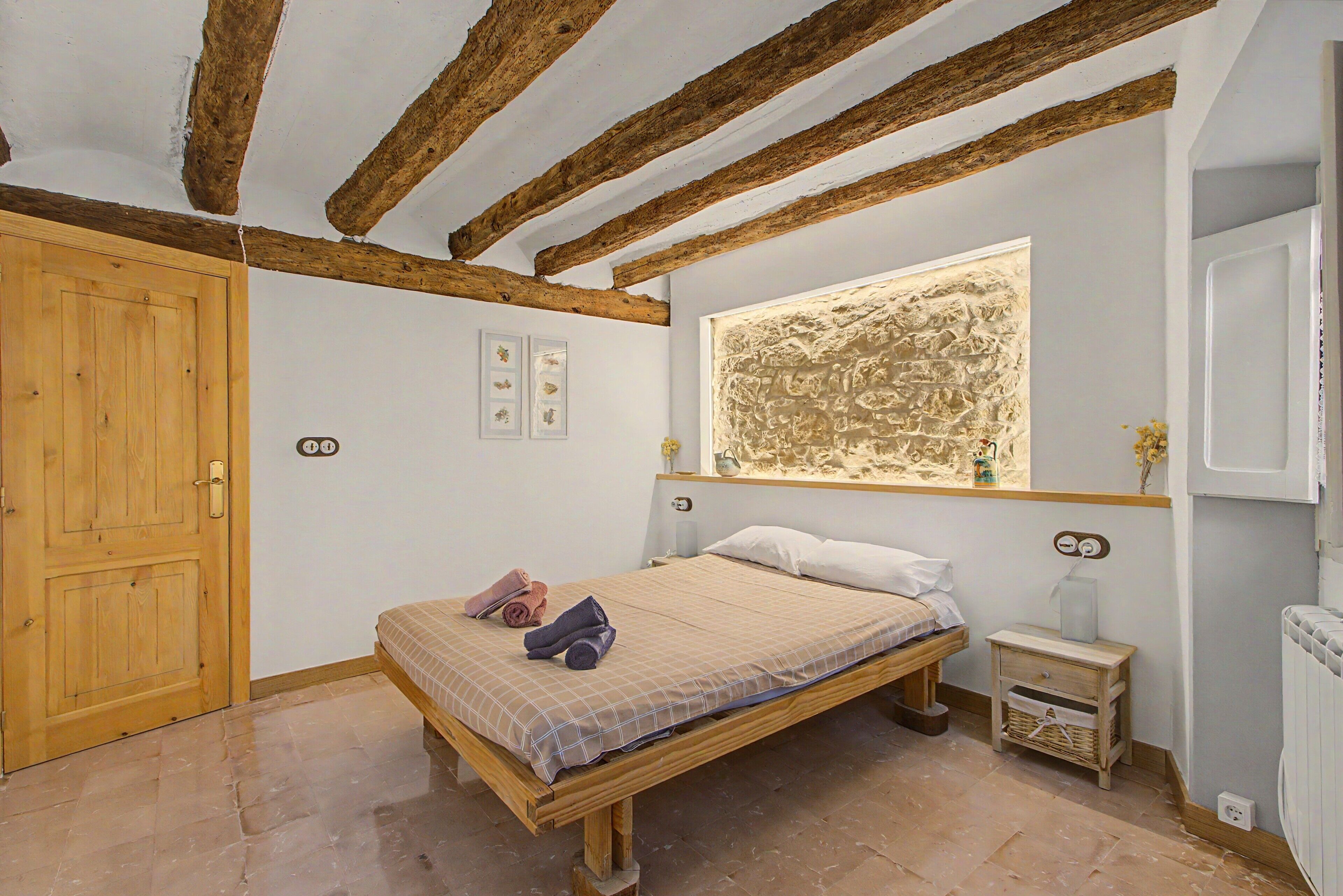 A bedroom with a wooden bed, a wooden wardrobe, a small bedside table, and a wall-mounted artwork.