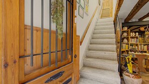 Una puerta de madera con una reja de metal, una escalera con barandilla de madera y una estantería llena de objetos varios.