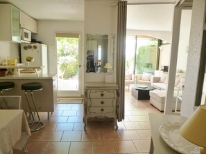 A modern kitchen with a dining area, a living room with a sofa, and a view of greenery outside. - Bright Apartment by the Ligurian sea (La Croix-Valmer)