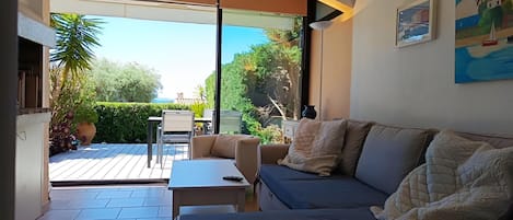 A modern living room with a sofa, a coffee table, and a dining table. There is a large window providing a view of the outdoors.