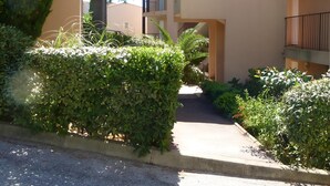 Un edificio residencial de varios pisos con balcones, un paseo techado y un jardín bien cuidado.