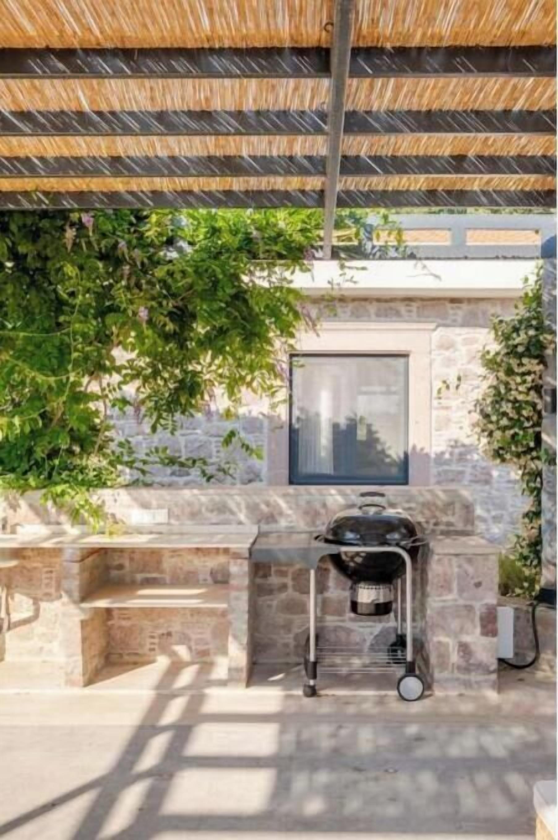 An outdoor grill area with a stone wall backdrop, a window, and a thatched roof structure.