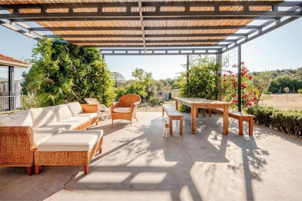 An outdoor patio area with wicker furniture, a wooden table, and a pergola structure.