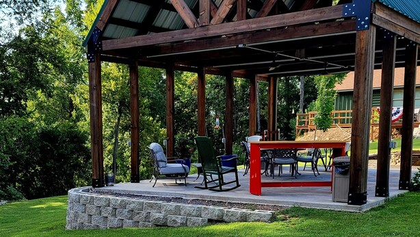 A covered outdoor seating area with stone steps, wooden beams, and a metal roof. - The Winchester Cabin —Rustic Warmth Meets Modern Comfort (Harriet)