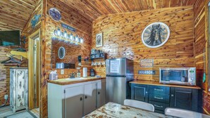 A rustic kitchen with wooden walls, a refrigerator, a microwave, and a clock. - The Winchester Cabin —Rustic Warmth Meets Modern Comfort (Harriet)