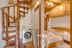 A compact room with a wooden spiral staircase, a washing machine, a bed with a striped bedspread, and wooden cabinets.