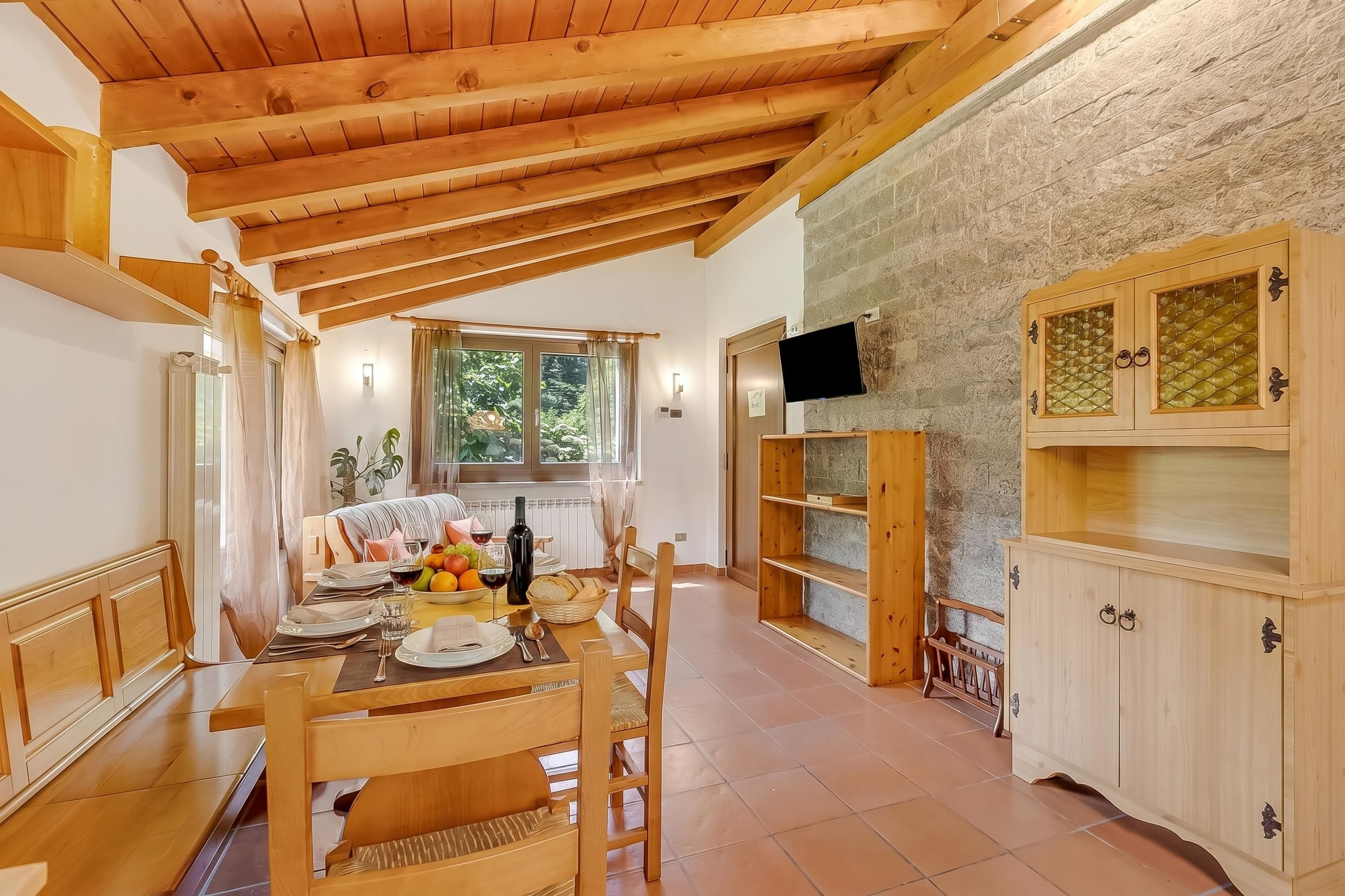 A dining area with a wooden table set for two, a stone wall, and a television mounted on the wall.