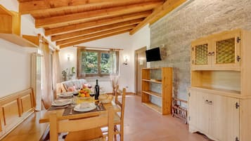 A dining area with a wooden table set for two, a stone wall, and a television mounted on the wall.