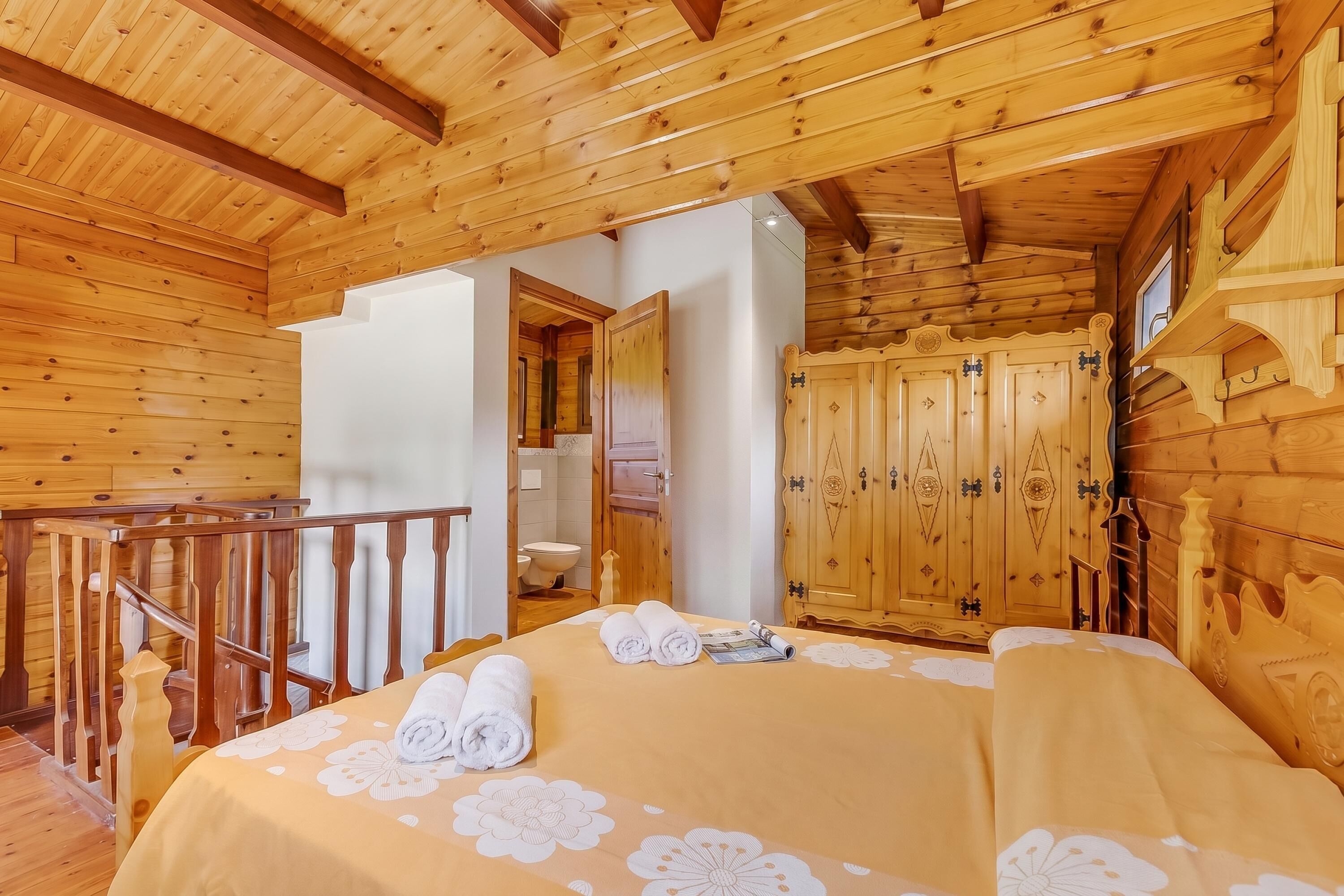 A wooden cabin interior with a bed, a bathroom, and a staircase.
