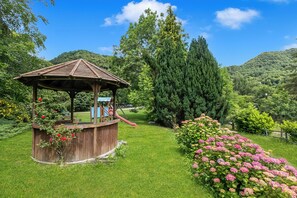 A wooden gazebo with a roof, surrounded by lush greenery and flowering plants. - Chalet La Gigliola (Laveno Mombello)