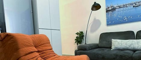 A living room with a sofa, a chair, a floor lamp, and a wall painting.