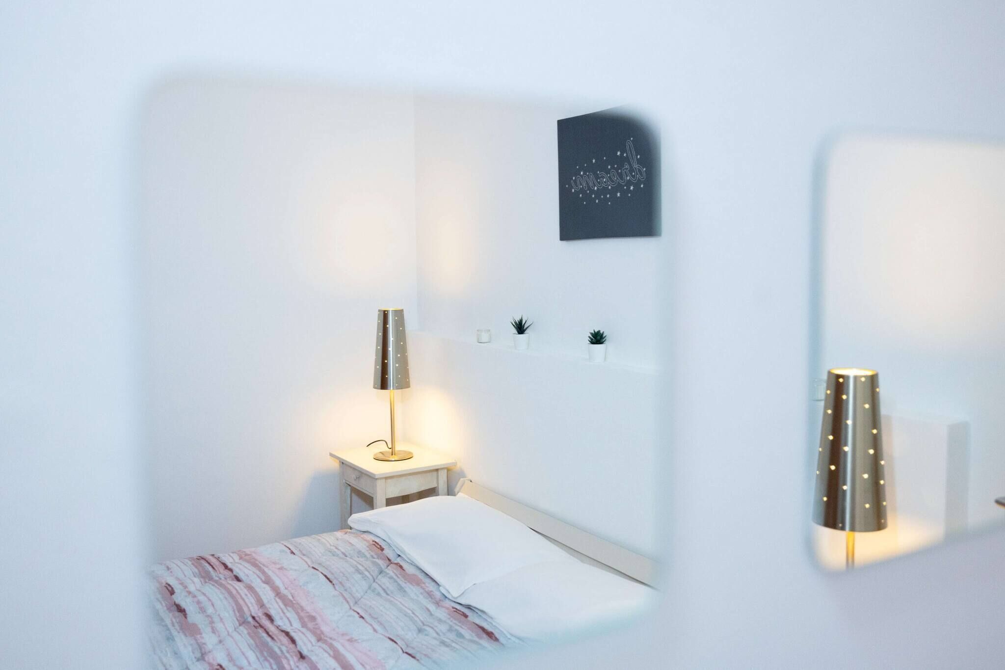A minimalist bedroom with a bed, bedside table, lamp, and wall-mounted decor.