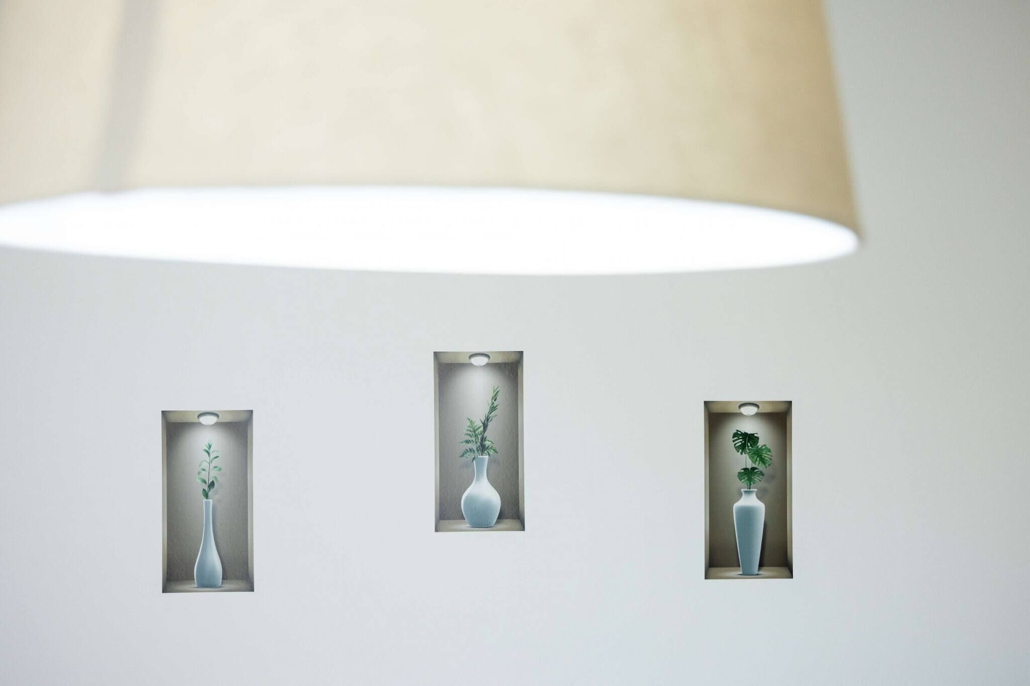 Three wall-mounted vases with plants under a large ceiling lamp.