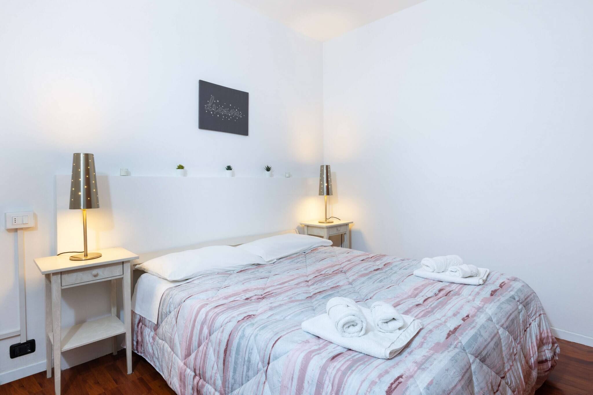A neatly made bed with a striped bedspread and two rolled towels on the side.