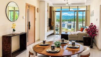 A modern living room with a dining area, a sofa, a TV, and a view of the outdoors.