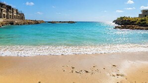 A beach with clear turquoise water, a sandy shore, and buildings on the left. - The Azure Suite Ocho Rios | 2BR (Ocho Rios)
